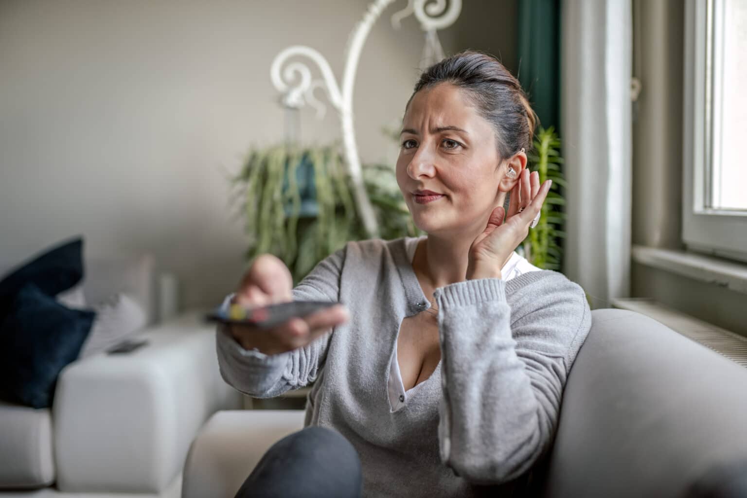 Woman adjusts her hearing aid while watching TV.