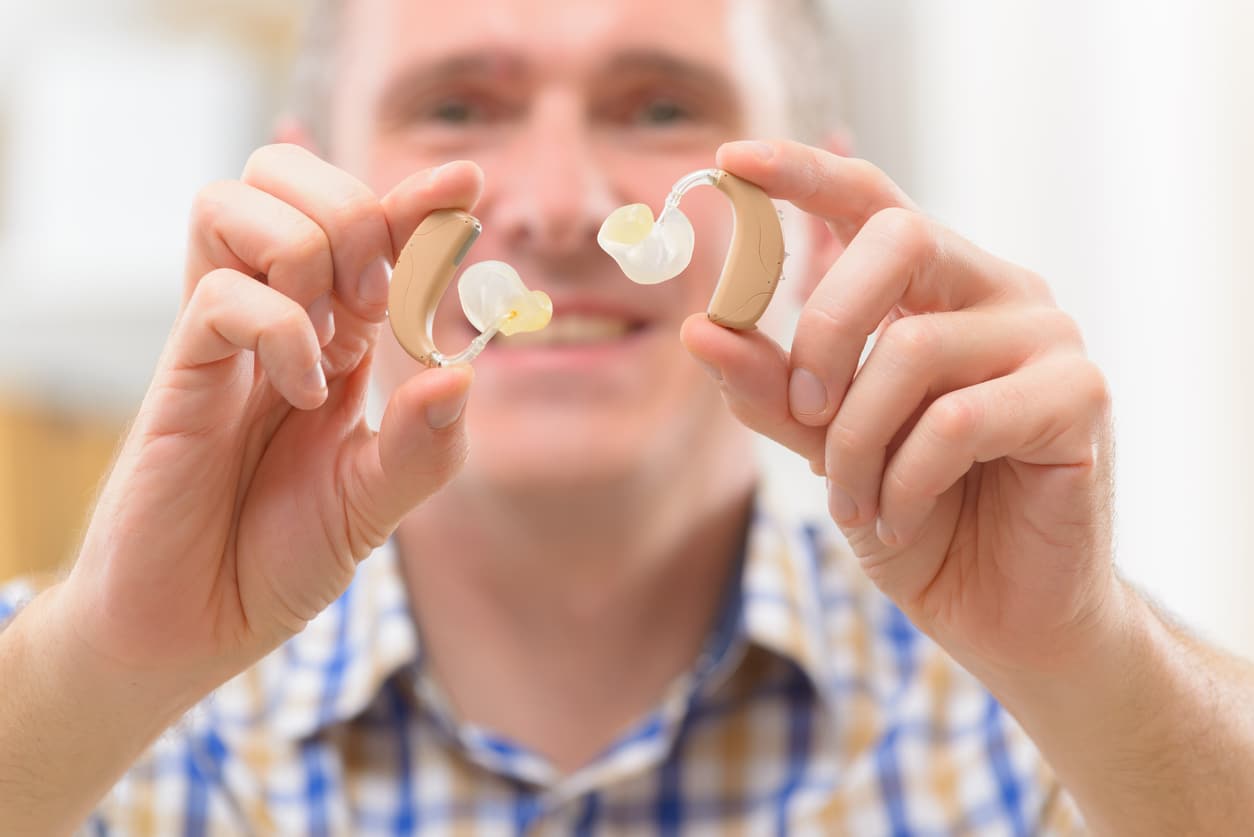 Man holding up two hearing aids.