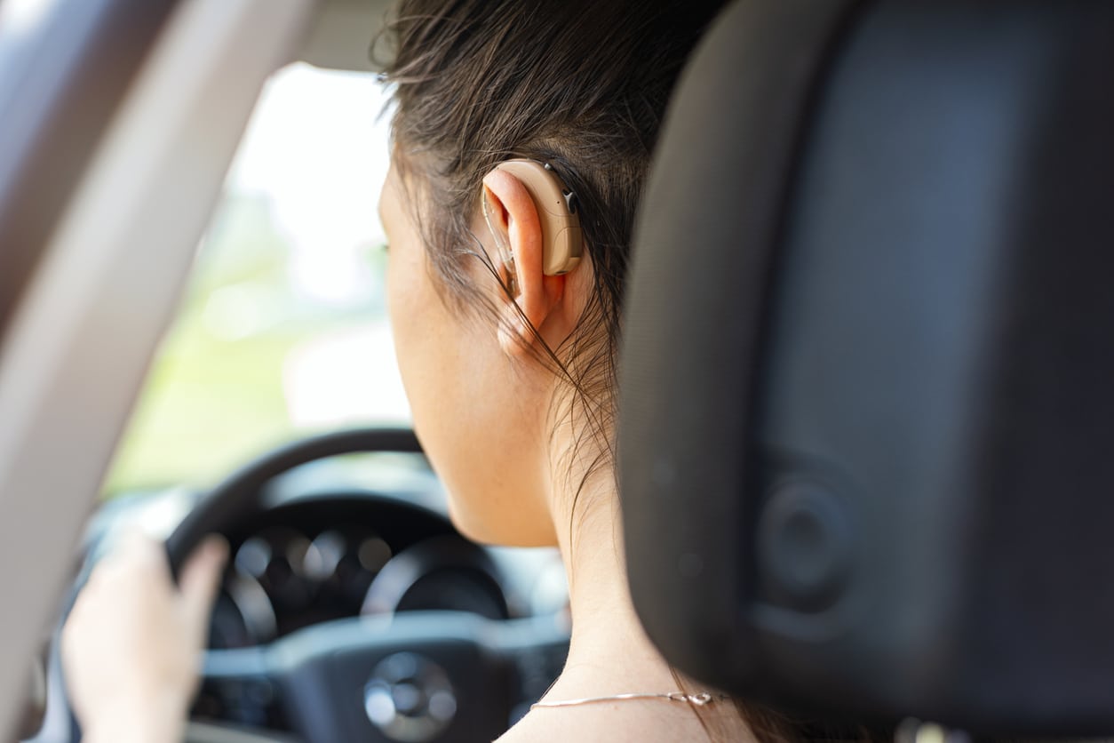 Woman wearing hearing aid while driving.