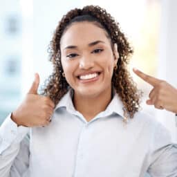 Smiling woman pointing to her new hearing aid