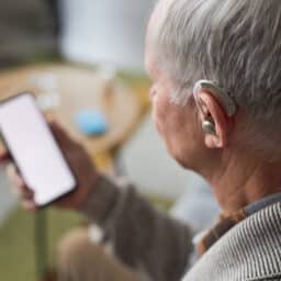 Senior man with a hearing aid looking at his phone.