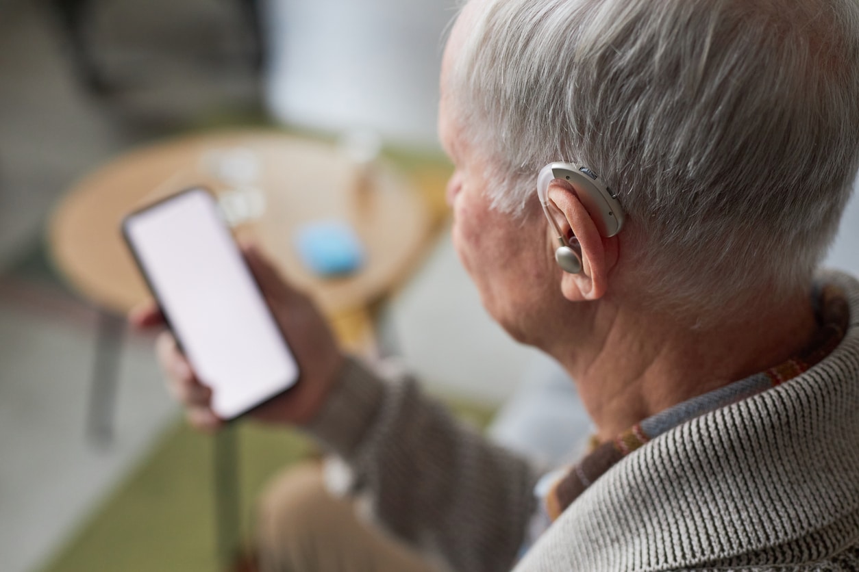 Senior man with a hearing aid looking at his phone.