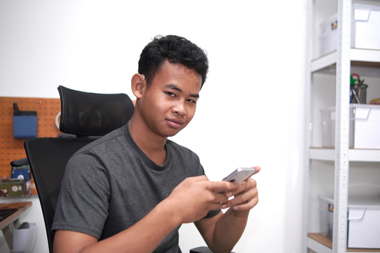 Young man wearing a hearing aid using his phone.